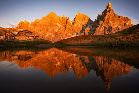 Cime dolomitiche illuminate dal tramonto riflesse in un lago alpino accanto al Rifugio Segantini. Acqua calma, luce calda e atmosfera serena.